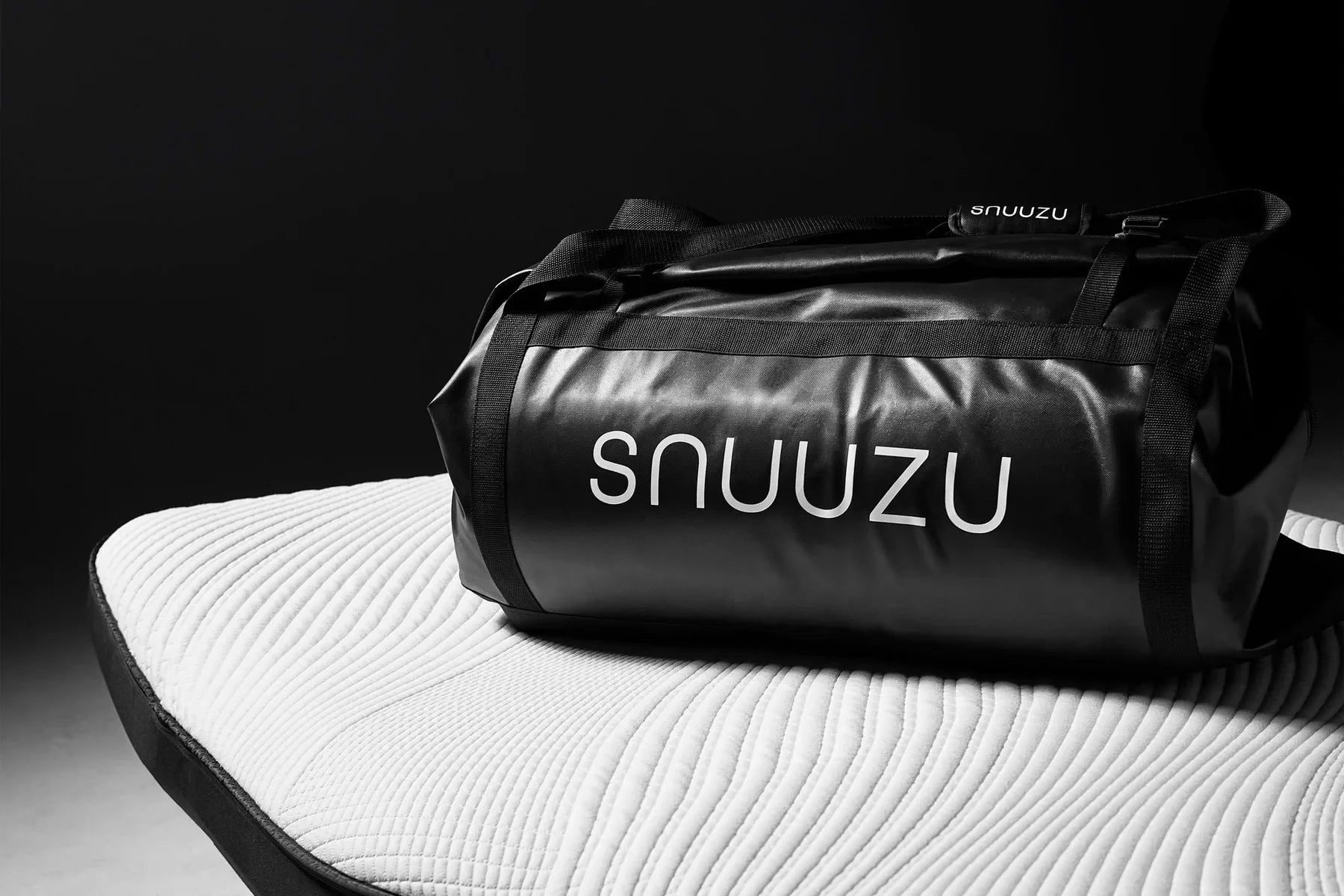 Black Snuuzu carry bag resting on a white quilted mattress