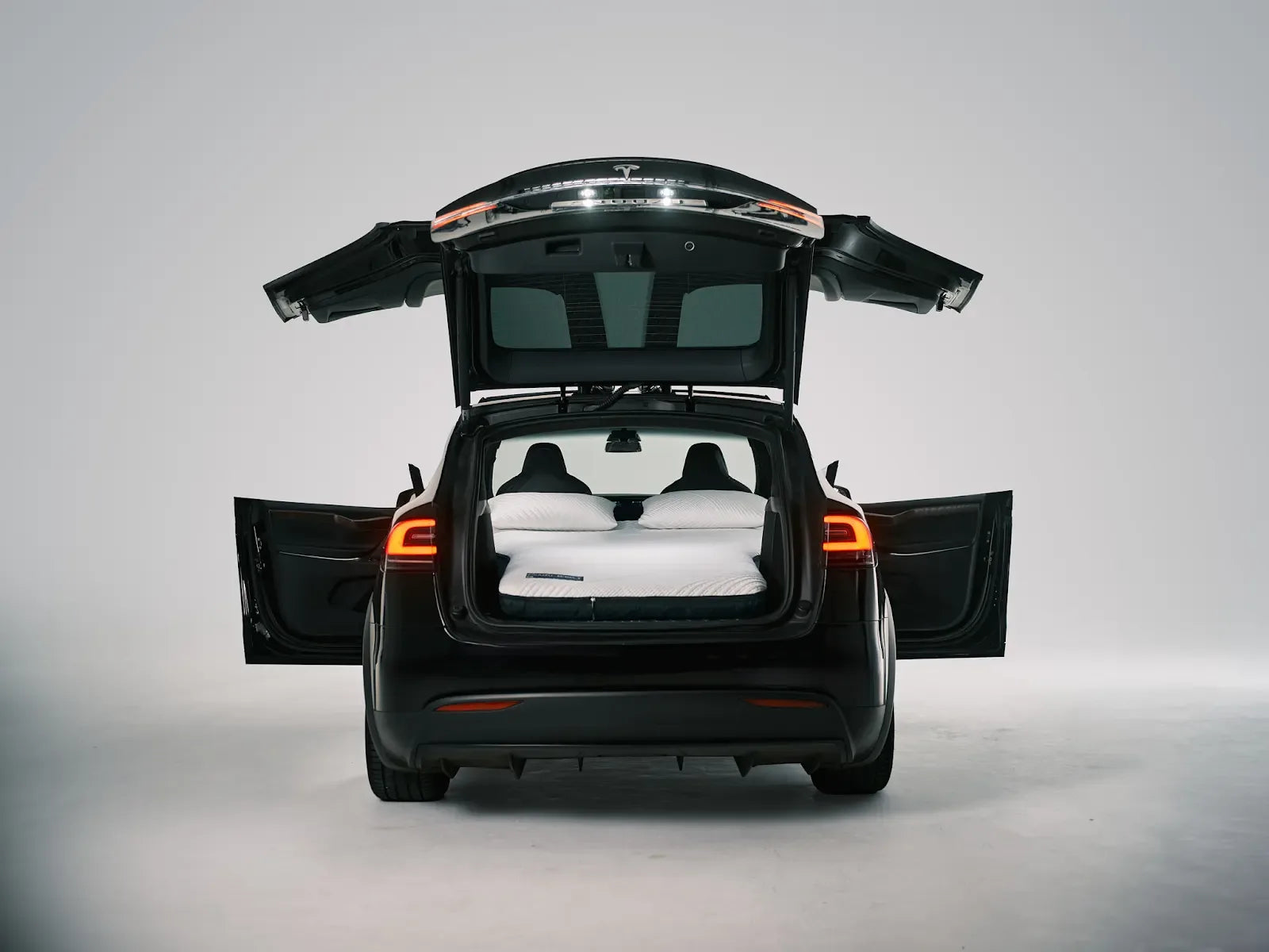 Tesla Model X with its hatch and Falcon Wing doors open around an installed two-pillow Snuuzu bed