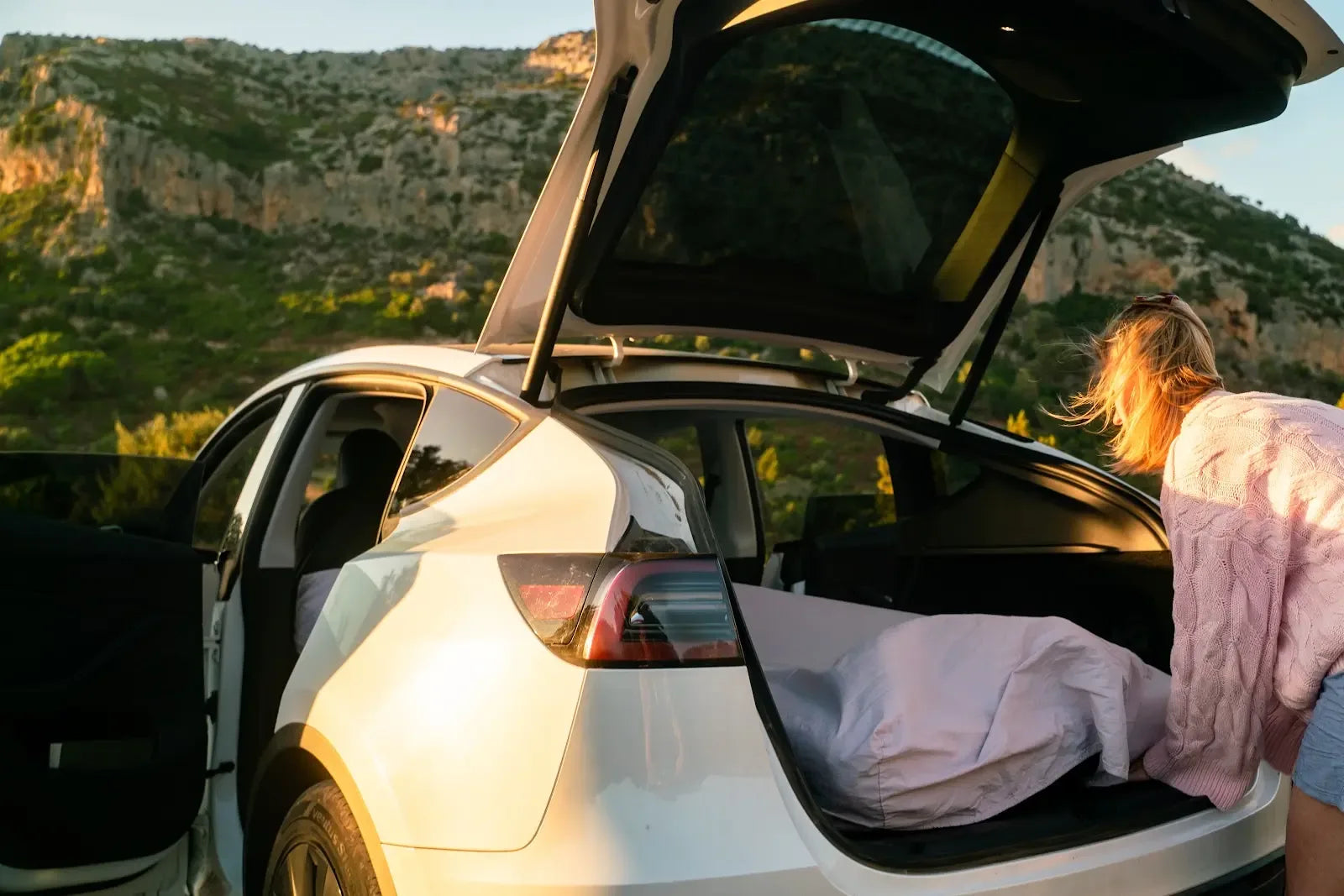 Camper arranging a Snuuzu bed through the open hatch of a Tesla Model Y at golden hour