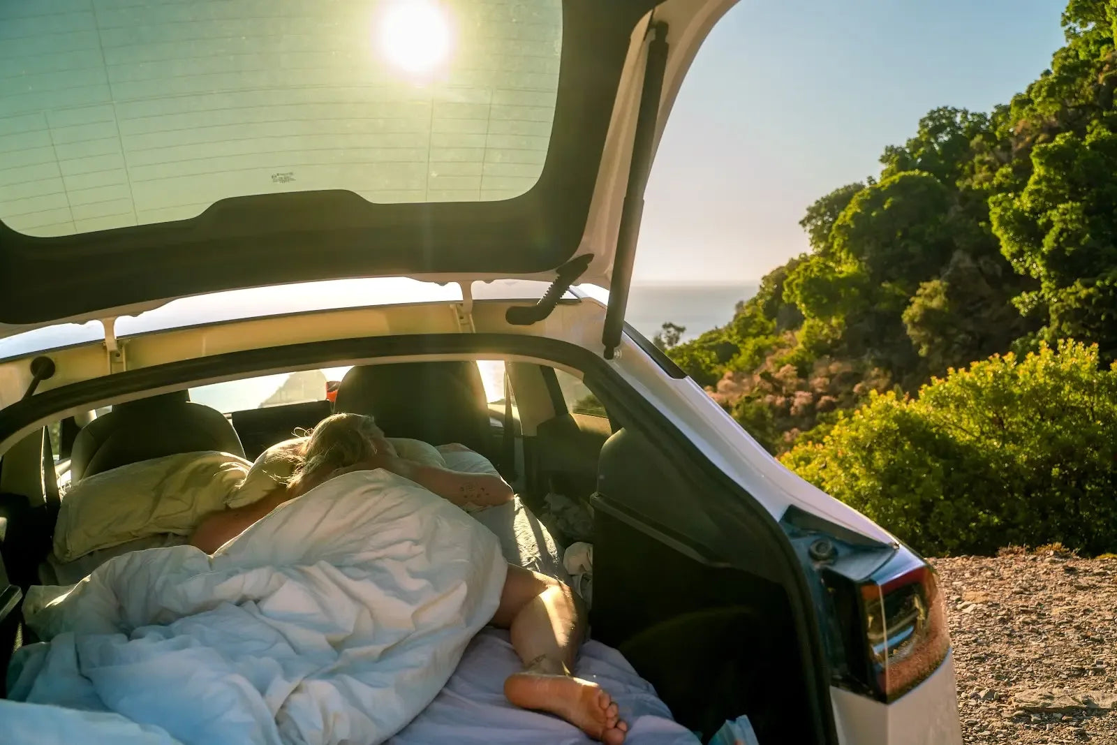 Camper resting under bedding on a Snuuzu mattress inside a Tesla Model Y