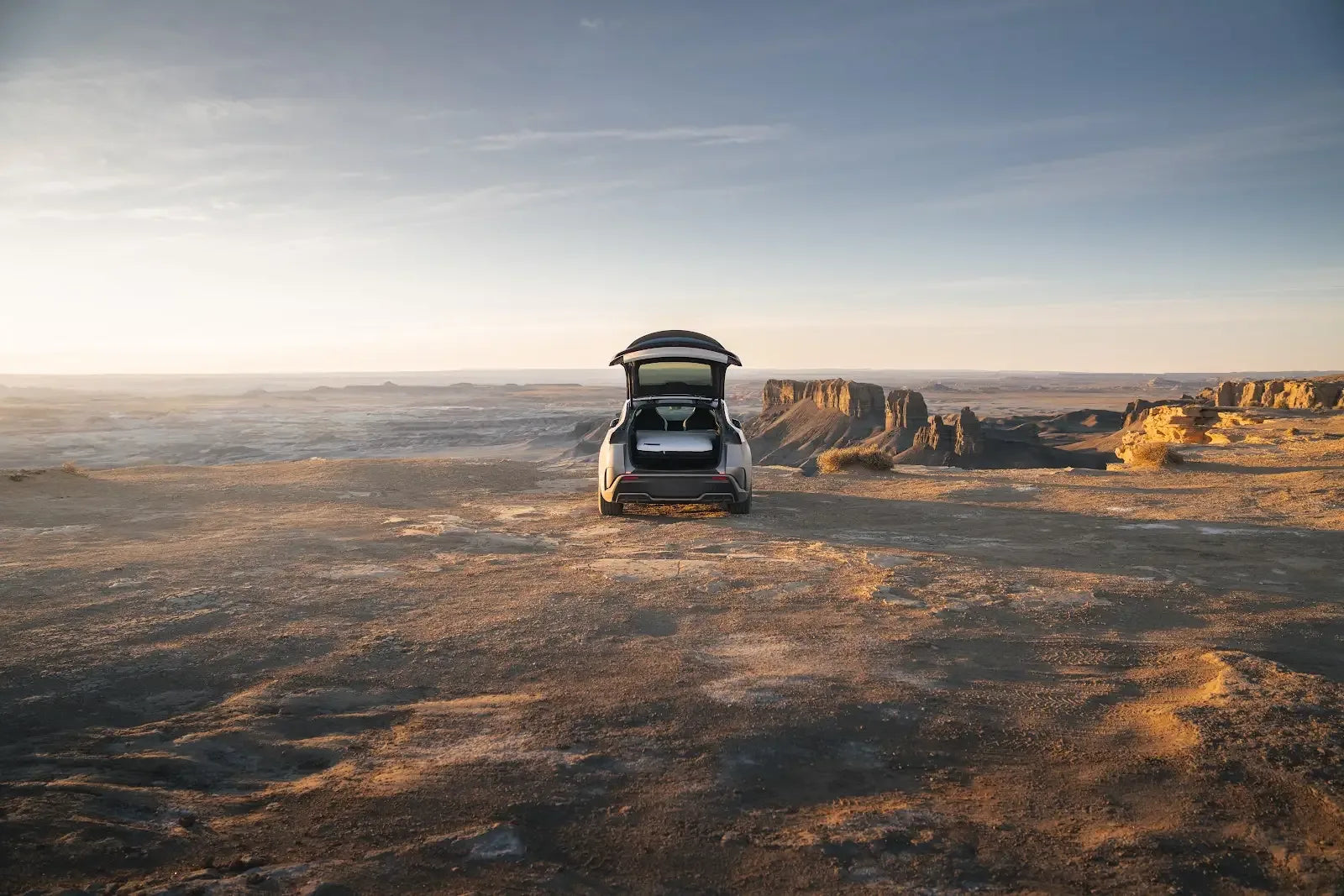 Tesla Model Y with its hatch open and a Snuuzu bed visible at a desert campsite