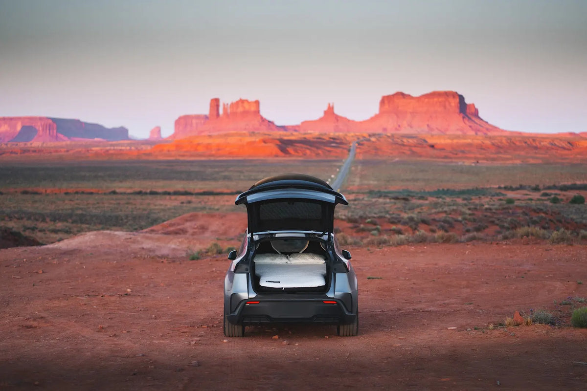 Tesla Model Y with an open hatch and Snuuzu bed beside a road through open countryside