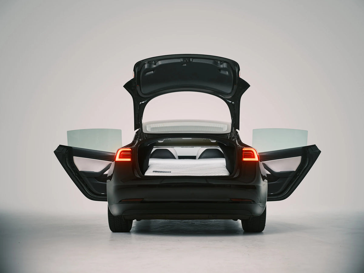 Tesla Model 3 with open trunk and rear doors, showing a Snuuzu mattress set up in the rear sleeping area.
